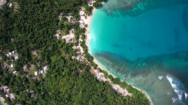 Aerial view of Mushu Island featuring a white sand beach, turquoise waters, and a small village nestled in dense jungle in Wewak District, East Sepik Province, Papua New Guinea.