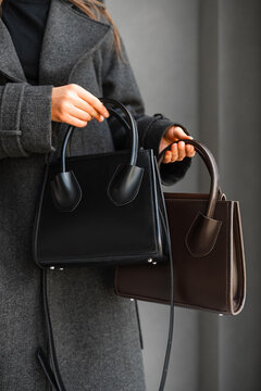 Close Up Woman Holding Black Handbag, Second Brown Satchel Draped Over Forearm, Wearing Tailored Grey Coat,