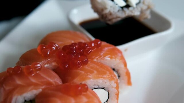Sushi roll dipped in soy sauce on black background close-up vertical video. Man eats sushi roll with chopsticks while soaking it in sauce. Philadelphia sushi with salmon