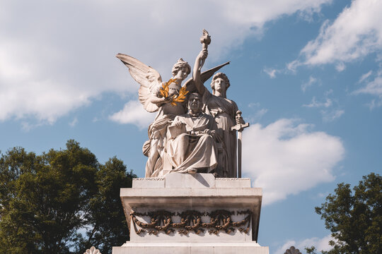 Majestic marble statue with angel and figures under blue sky in park setting during daytime