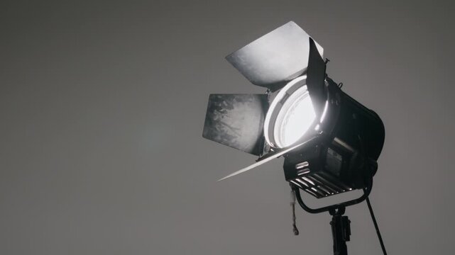 Professional Fresnel film studio light with open barn doors glowing brightly against a neutral gray backdrop symbolizing cinema production filmmaking creativity and the spotlight moment