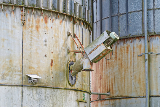 Rusty industrial metal silos with machinery and weathered surfaces outdoors