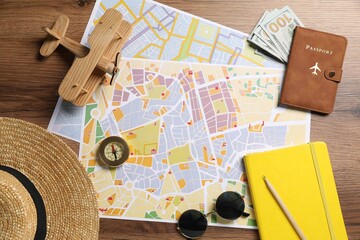 Obraz premium Planning trip. City maps, compass, dollars, sunglasses, passport, stationery, straw hat and toy plane on wooden table, flat lay
