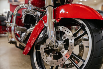 Fototapeta premium Detailed view highlights front wheel, tire, brake disc, and chrome components of red motorcycle. Low-angle perspective emphasizes robust engineering and polished surfaces in showroom setting.
