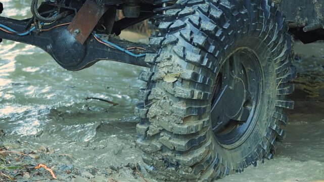 Close up action shot of large 4x4 tire spinning through wet dirt and water. Dynamic view of suspension and axle during extreme motorsports event. Conveys power, adventure, and challenge