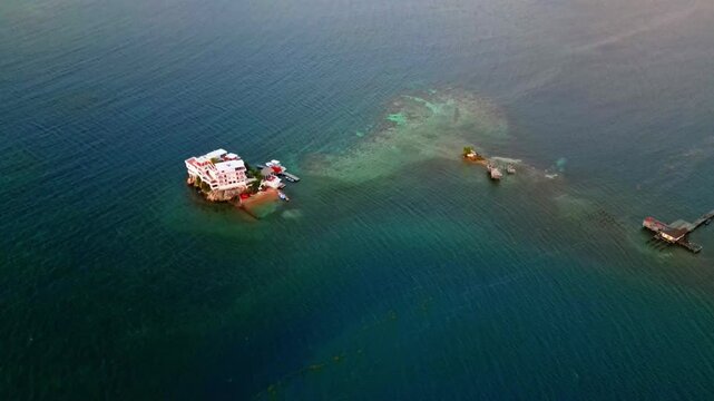 Aerial view of a white building on a rocky islet surrounded by turquoise water and coral reefs in Sandy Bay, Bay Islands Department, Honduras.
