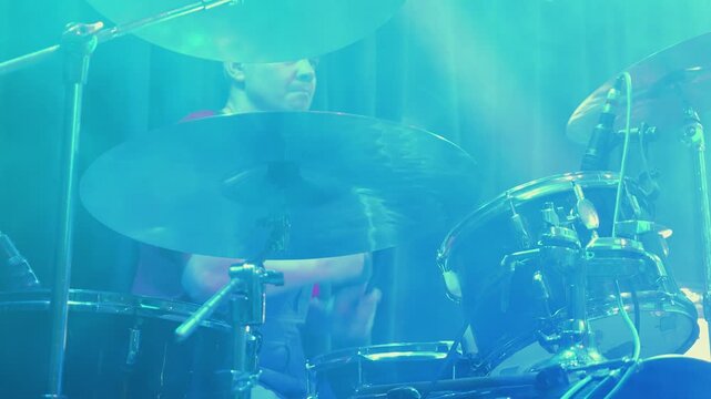 Close up of drummer playing drum kit on stage. Colorful pink and yellow lights create atmospheric haze during live rock concert. Dynamic shot captures energy of musical performance and rhythm