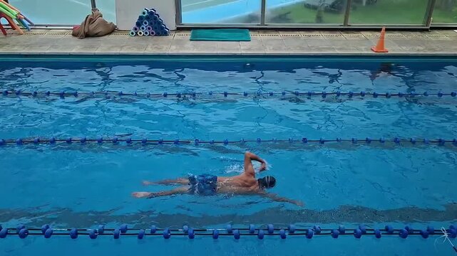 Professional swimmer practicing front crawl technique in a blue indoor pool; 4K horizontal side-view of athletic training, fitness, and aquatic sports.