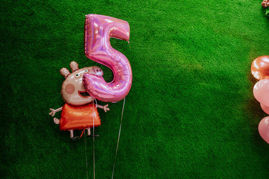 Peppa Pig character balloon alongside a large pink number 5 balloon on a vibrant green grass backdrop for a birthday celebration