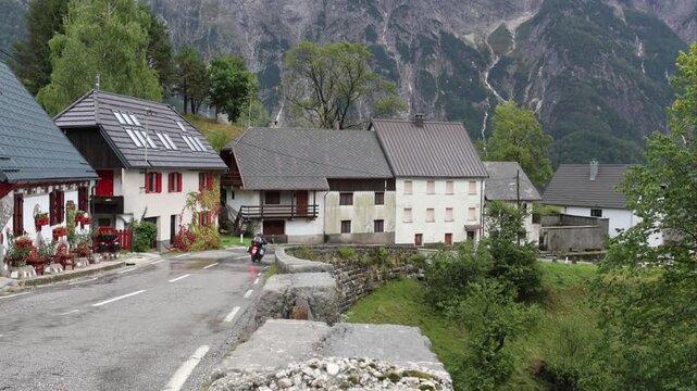 motorcycle driving down wet rainy road in small village on the italian slovenia border in the julian alps (slovenia europe) european travel destination touring houses town