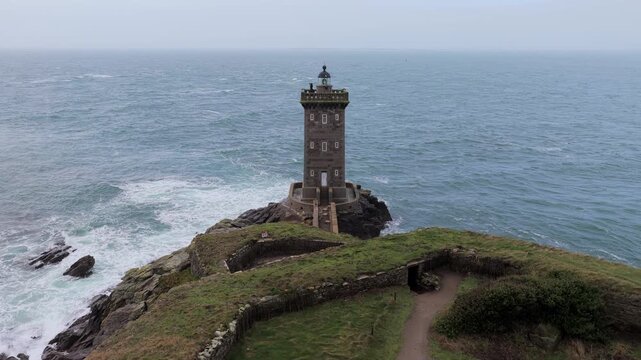 Aerial view of Kermorvan Lighthouse standing on a rugged rocky peninsula surrounded by the Atlantic Ocean waves in Le Conquet, Bretagne, France.
