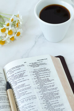 Open holy bible book, cup of coffee and spring flowers on white marble background. Christian scripture study, biblical concept.