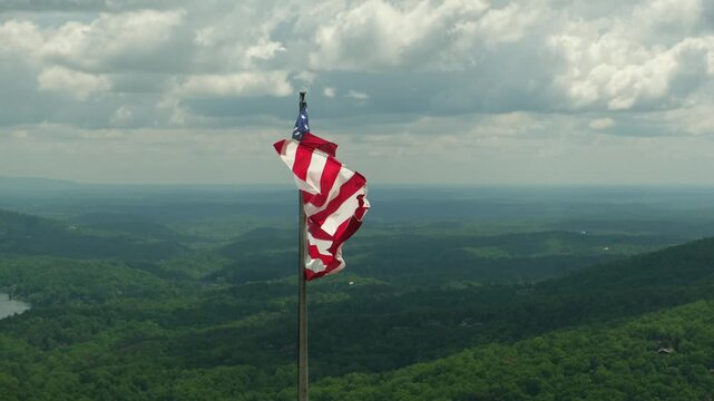 an American flag fluttering in the wind against a backdrop of a picturesque valley and clouds