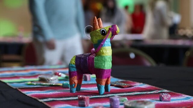 A miniature pinata on top of a table surrounded by candy as party lights flash around it. 