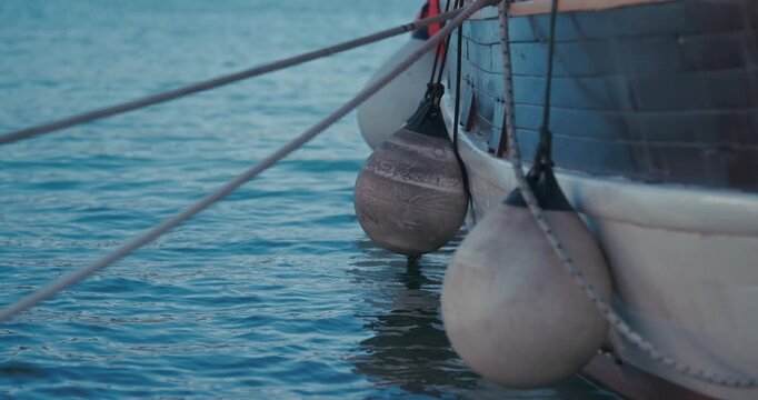 Close up of boat fenders hanging beside a moored wooden boat on calm harbor water in Rovinj, Croatia.