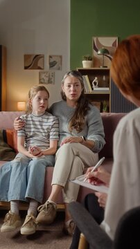 Vertical shot of adult mother discussing young daughters cough and fever symptoms with female pediatrician while doctor taking notes during house call