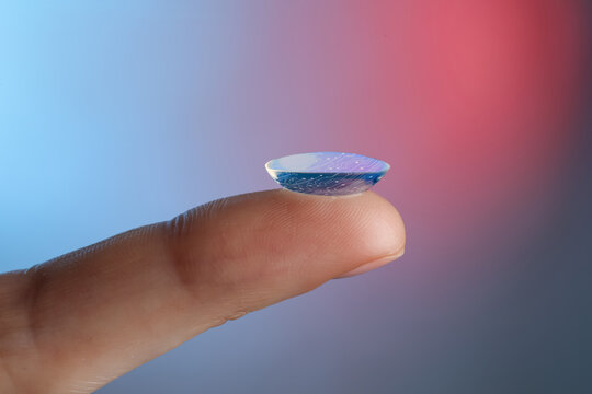 Contact lenses of future. Woman holding lens with digital implants on color background, closeup