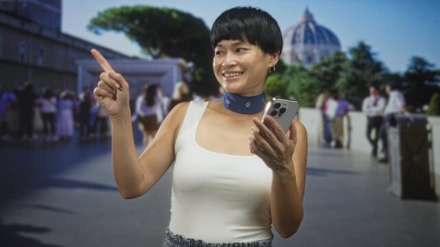 Woman holding smartphone points finger at historic building entrance while smiling and wearing choker and tanktop; travel curiosity joy.