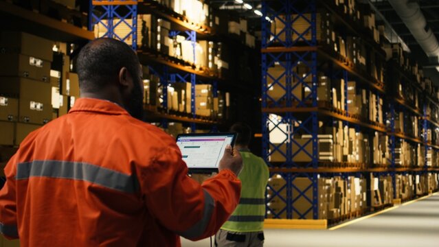 Black worker verifying cargo with tablet and scanner for shipment in depot. Supply chain operations combine manual labor and tracking to ensure efficient parcel dispatch and transportation.