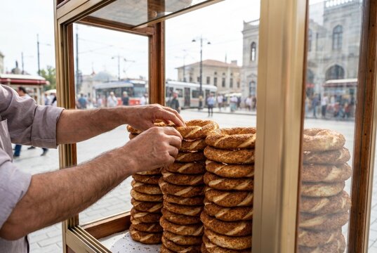 Street vendor arranging fresh sesame simit bread rings inside a glass display cart in a city square
