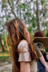 Fototapeta premium Woman with long hair in forest nature, casual backpack and walk with friend, side portrait and redhead profile in dappled daylight among trees and green woodland background.
