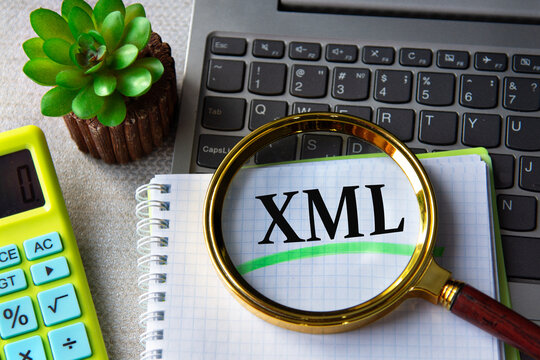 XML acronym in notebook under magnifying glass with laptop and calculator in background