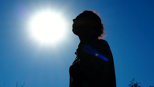 Woman drinking water under the sun silhouette. Silhouetted female standing against bright sky, drinking water while battling intense summer heat and seeking refreshment from scorching sunlight