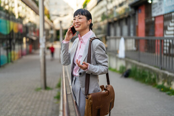 Fototapeta premium Asian businesswoman talking on smart phone outdoors in city