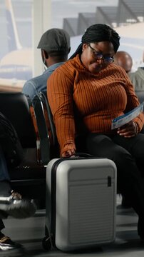 Vertical video Chatting, going to boarding gate and African American woman in airport hub. Standing up from chairs, talking and travelers in lounge interrupted by boarding call during discussion