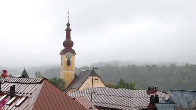 rain falling in the julian alps mountains in tarvisio, italy on the border with slovenia church rooftops trees hills mist weather raining storm alpine travel destination