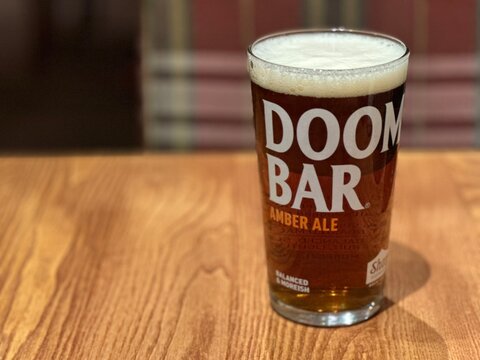 Norwich, UK - January 30, 2026: A pint of Doom Bar amber ale in a branded glass on a wooden table in a pub. 