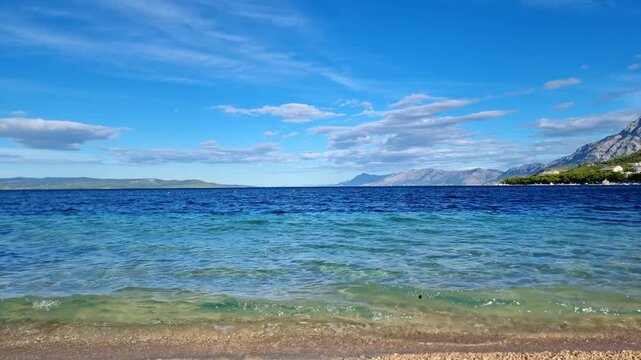 The turquoise water of the Adriatic Sea breaking on a pebble beach from beautiful Makarska riviera, Croatia, in sunny summer day
