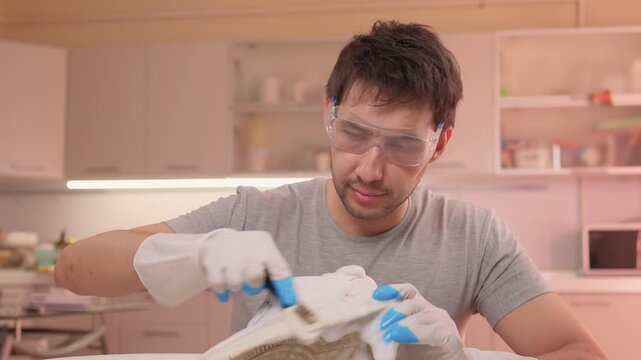 Homeowner cleans sneaker soles carefully. Sponge removes dirt from textured shoe soles. Closeup of homeowner washing sneaker soles using sponge and soapy water in sink