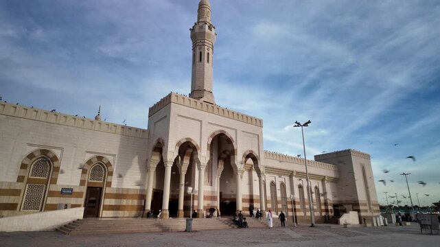 Muslim pilgrims in square with pigeons flying in front of Masjid Sayyid al-Shuhada of in holy city Medina of Saudi Arabia, during sunset, one of the most important mosques in the world