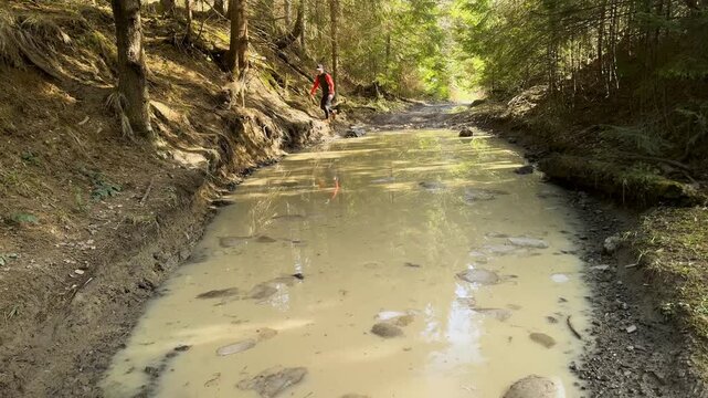Trail runner athlete running through a large puddle with ice on a mountain forest road in Carpathians. Active lifestyle, extreme sports and endurance concept. Professional runner in spruce forest.