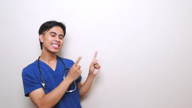 Joyful Asian male nurse in blue scrubs smiling and pointing at copy space for healthcare advertisement or medical presentation.