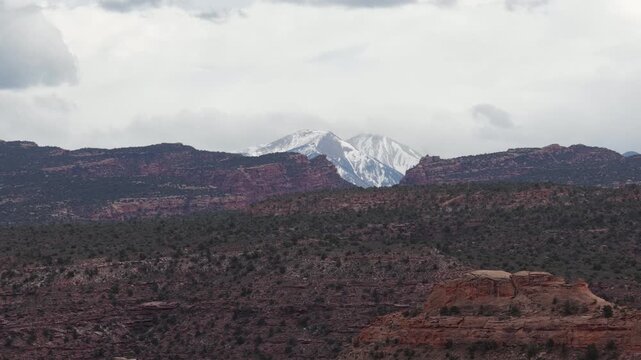 Zoom aerial view of snow capped La Sal Mountains in Moab Utah in spring with cloudy sky