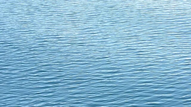 4K HD video flying above calm rippling blue water.
