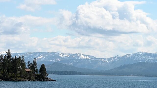 4K HD Video panning from forested river bank to snow capped mountains along the shoreline of Lake Tahoe. View from the water.
