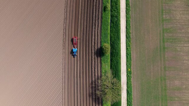 Aerial view of a blue tractor working in a ploughed field with straight furrows and green verges in Knottingley, England, United Kingdom.