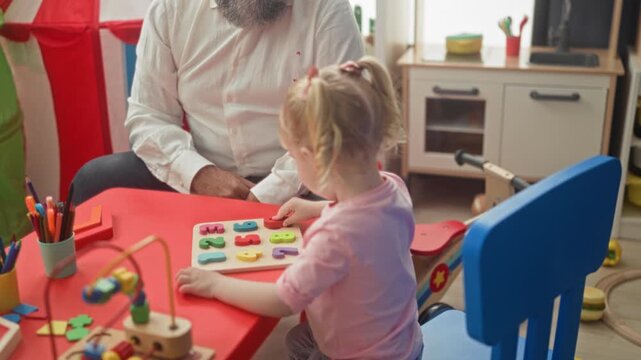Little girl places wooden number pieces on a red table puzzle, hand reaching and pointing, man nearby in building; curious learning care.