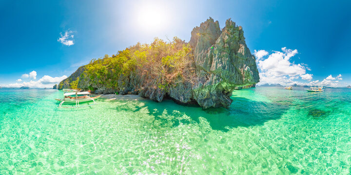 360 view of White sand beach at Entalula, El Nido, Palawan with swaying palms, turquoise water, traditional bangka boats and dramatic limestone karsts beneath a blue sky with clouds in Philippines,