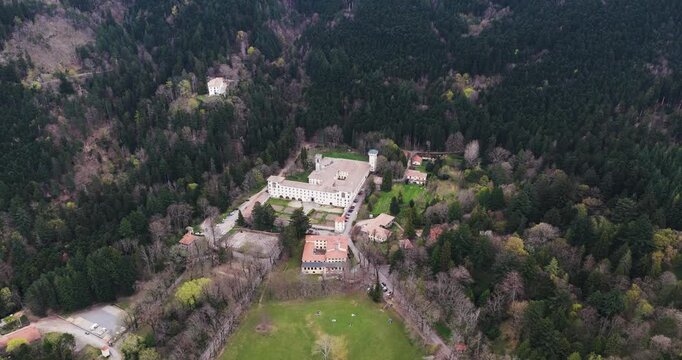 Aerial view of the historic Vallombrosa Abbey surrounded by a vast forest of tall trees and green meadows in Vallombrosa, Tuscany, Italy.
