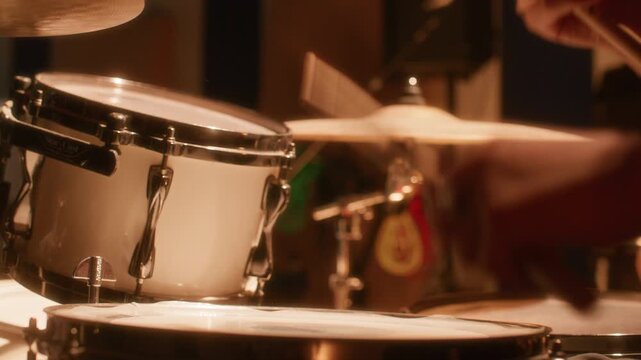 Hands of professional female drummer playing drum kit during recording session in music studio filled with warm light. Close up view