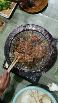 People Grilling Sliced Beef with Chopsticks on Korean BBQ Pan