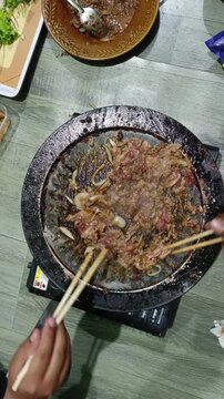 Cooking Sizzling Beef and Onions on a Round BBQ Grill with Chopsticks