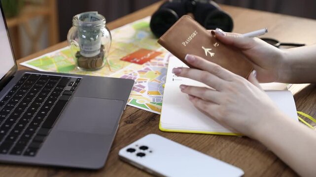Woman with passport and laptop planning trip at table, closeup