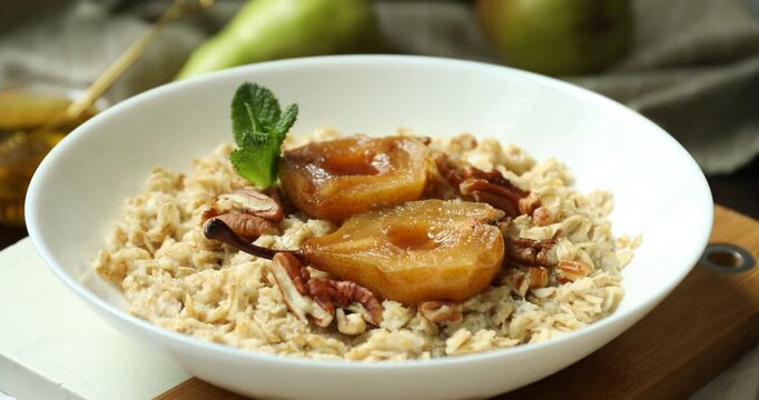 Tasty oatmeal porridge with caramelized pear, nuts, mint and fresh fruits on table, closeup