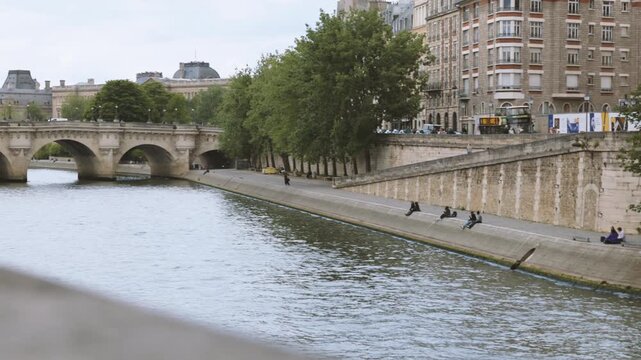 Panning shot of people sitting by the Seine River near Pont Neuf in Paris