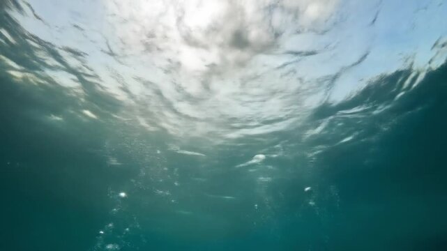 Underwater view light rays penetrate the water creating a rippled surface Air bubbles rise upwards